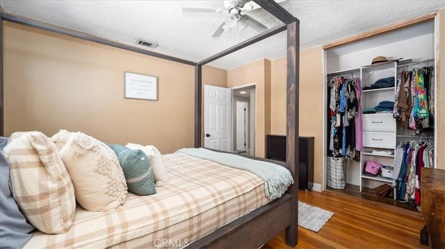 bedroom featuring a closet, a textured ceiling, a ceiling fan, visible vents, and wood finished floors