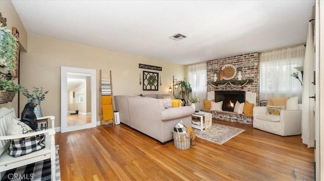 living area featuring visible vents, a brick fireplace, wood finished floors, and baseboards