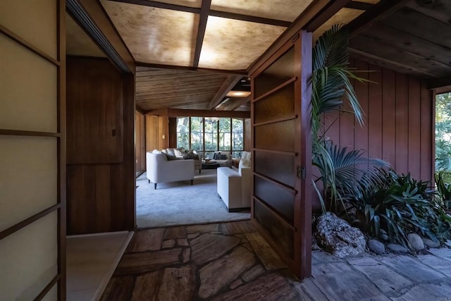 hallway featuring wooden walls, vaulted ceiling, and a healthy amount of sunlight