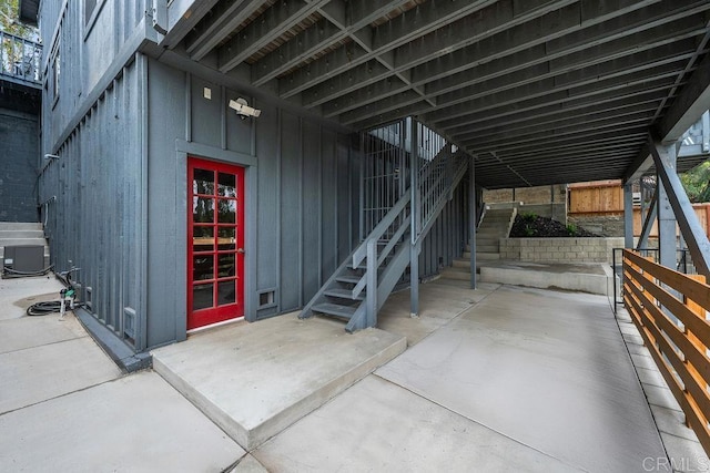 view of exterior entry featuring board and batten siding, central AC, and a patio