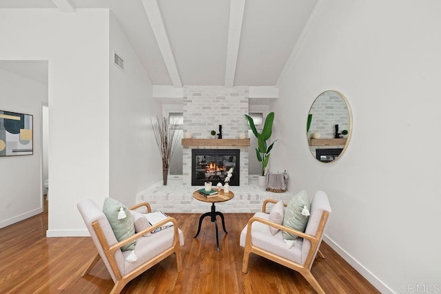 living area with vaulted ceiling with beams, visible vents, baseboards, wood finished floors, and a brick fireplace