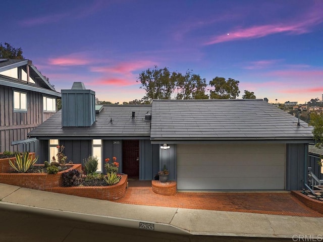 view of front of property with board and batten siding, an attached garage, a chimney, and decorative driveway