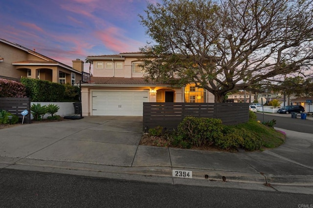 traditional-style house with stucco siding, fence, a tile roof, an attached garage, and concrete driveway
