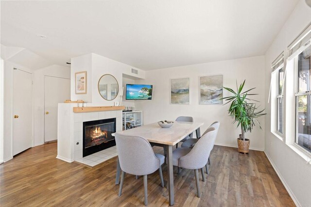 dining area featuring a tiled fireplace, visible vents, baseboards, and wood finished floors