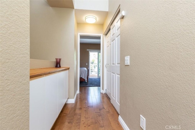 hall featuring hardwood / wood-style floors, a textured wall, and baseboards