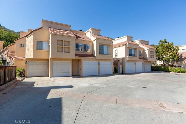 multi unit property featuring stucco siding, driveway, an attached garage, a tiled roof, and fence