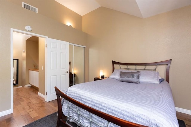 bedroom featuring visible vents, baseboards, a closet, wood finished floors, and lofted ceiling
