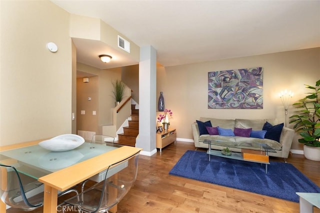 living room with visible vents, baseboards, light wood-style floors, and stairs