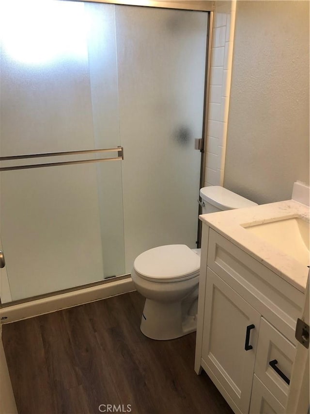 full bath featuring a shower stall, wood finished floors, vanity, and toilet