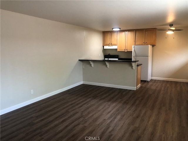 kitchen with baseboards, a ceiling fan, freestanding refrigerator, a peninsula, and under cabinet range hood