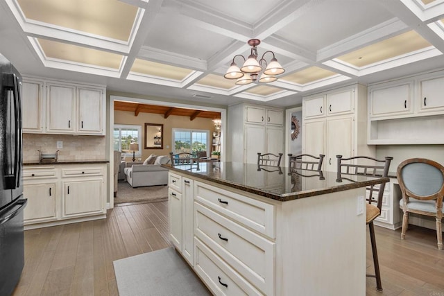 kitchen featuring freestanding refrigerator, beam ceiling, a kitchen breakfast bar, hardwood / wood-style floors, and a chandelier