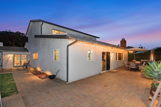 back of property at dusk with a chimney, a patio area, outdoor dining space, and stucco siding