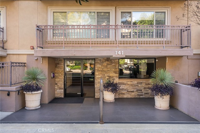 view of exterior entry with a balcony, stucco siding, and stone siding