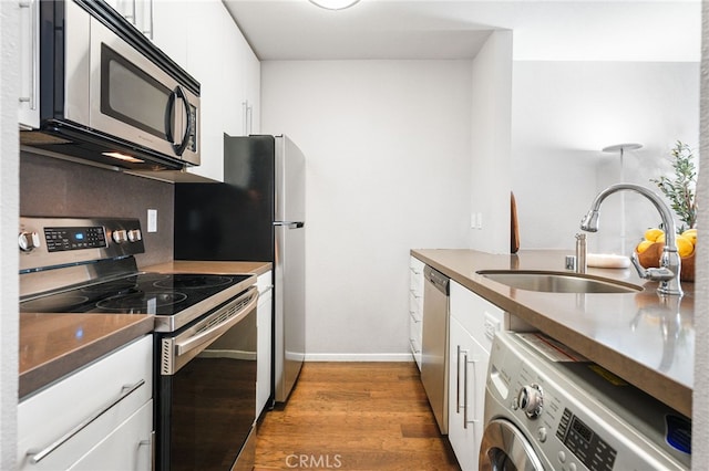 kitchen with washer / clothes dryer, white cabinetry, wood finished floors, a sink, and stainless steel appliances