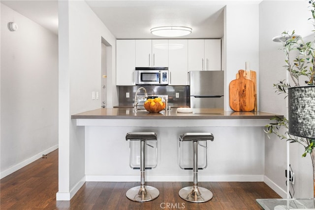 kitchen featuring tasteful backsplash, a peninsula, dark wood-type flooring, a kitchen bar, and appliances with stainless steel finishes