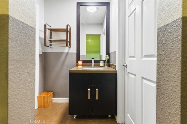 bathroom featuring a textured wall, tile patterned floors, vanity, and baseboards