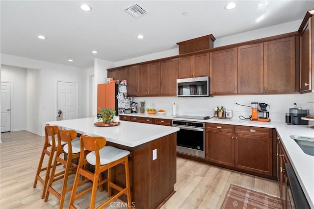 kitchen featuring a breakfast bar, a center island, visible vents, appliances with stainless steel finishes, and light wood finished floors