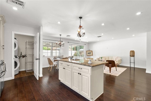 kitchen featuring light stone countertops, a notable chandelier, stacked washing maching and dryer, and baseboards