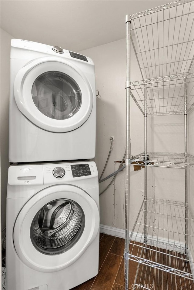 laundry area featuring stacked washing maching and dryer, wood tiled floor, laundry area, and baseboards