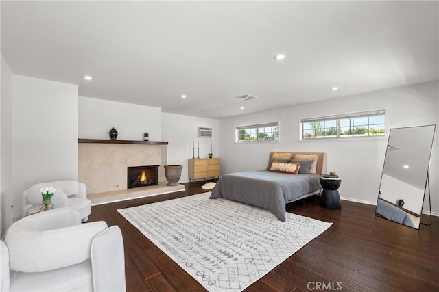 bedroom with dark wood-style flooring, visible vents, recessed lighting, and a warm lit fireplace