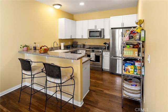 kitchen with a peninsula, white cabinets, dark wood-type flooring, appliances with stainless steel finishes, and a sink