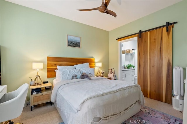 bedroom with a ceiling fan, connected bathroom, a barn door, and light carpet