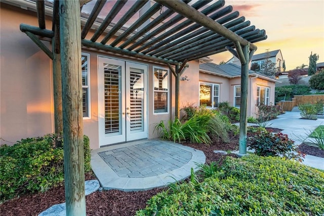 exterior entry at dusk with french doors, a patio, stucco siding, and fence