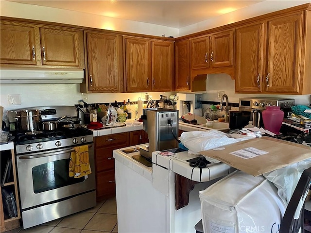 kitchen featuring brown cabinetry, range hood, tile countertops, and stainless steel range with gas stovetop