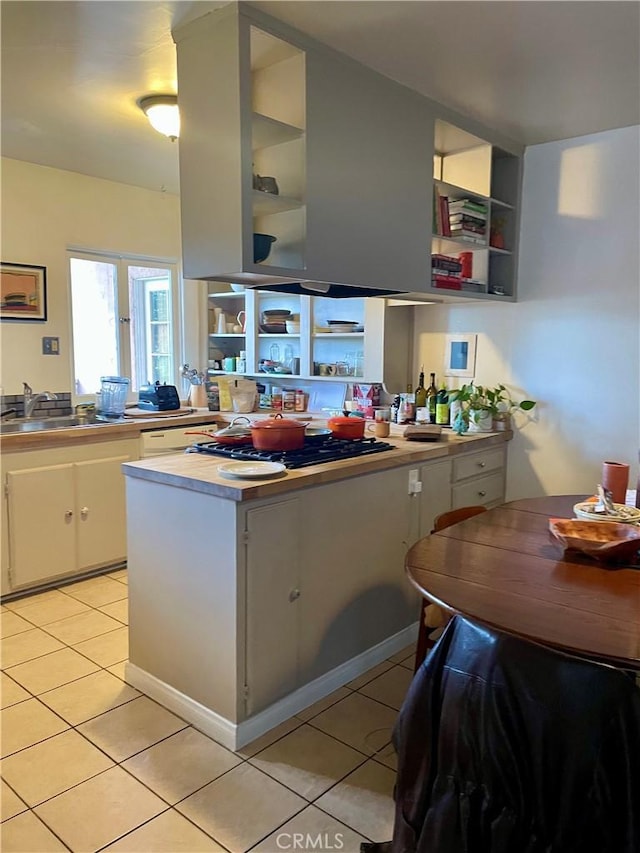 kitchen with light tile patterned floors, open shelves, white cabinets, light countertops, and a sink