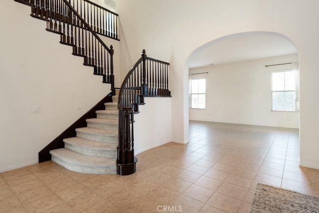 stairs with tile patterned floors, arched walkways, and baseboards
