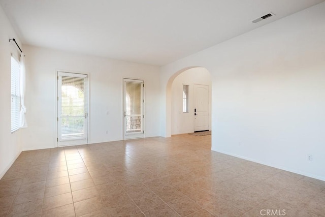 spare room featuring arched walkways, light tile patterned floors, visible vents, and baseboards