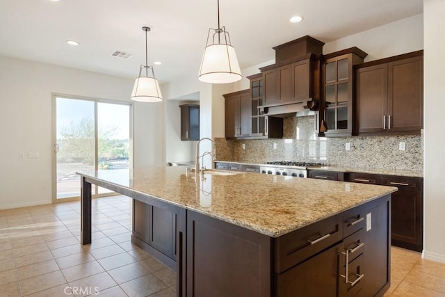 kitchen featuring light stone counters, a kitchen island with sink, visible vents, decorative backsplash, and a sink