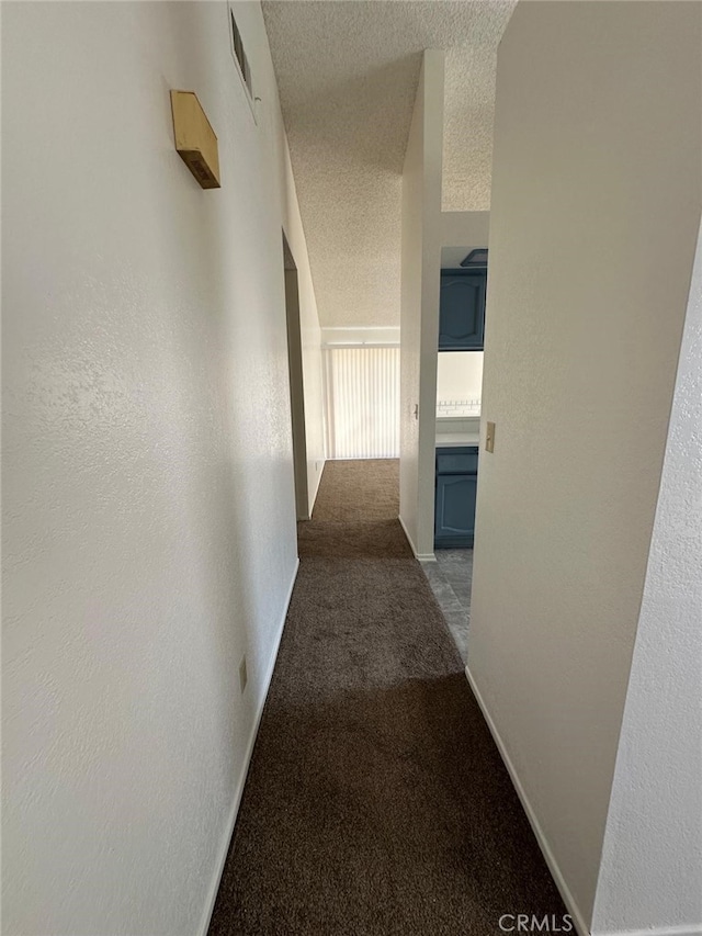 hall with a textured wall, carpet floors, visible vents, and a textured ceiling