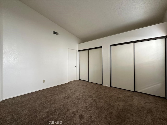 unfurnished bedroom featuring multiple closets, carpet, baseboards, lofted ceiling, and visible vents