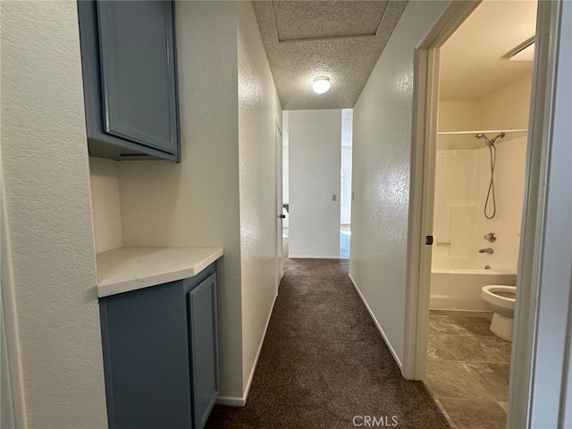hallway featuring baseboards, a textured wall, dark colored carpet, and a textured ceiling