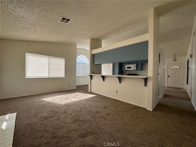 unfurnished room with a textured ceiling, dark colored carpet, and visible vents