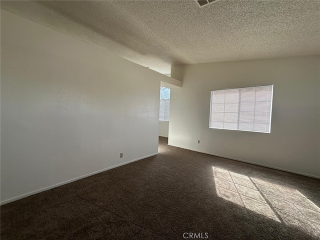 spare room featuring baseboards, dark colored carpet, and a textured ceiling