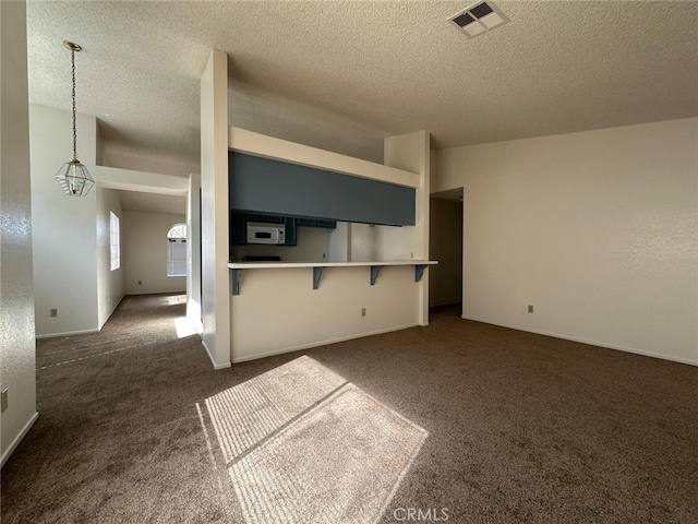 unfurnished living room with a textured ceiling, dark colored carpet, and visible vents