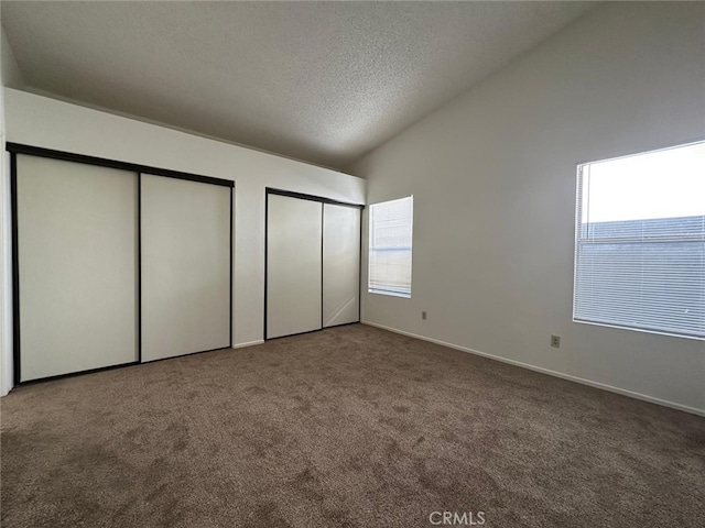 unfurnished bedroom with multiple closets, vaulted ceiling, carpet floors, baseboards, and a textured ceiling