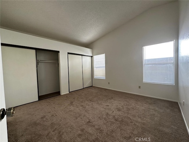 unfurnished bedroom featuring a textured ceiling, carpet, multiple closets, and lofted ceiling