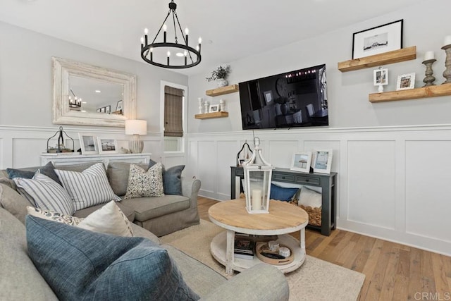 living room featuring a decorative wall, wood finished floors, a chandelier, and wainscoting