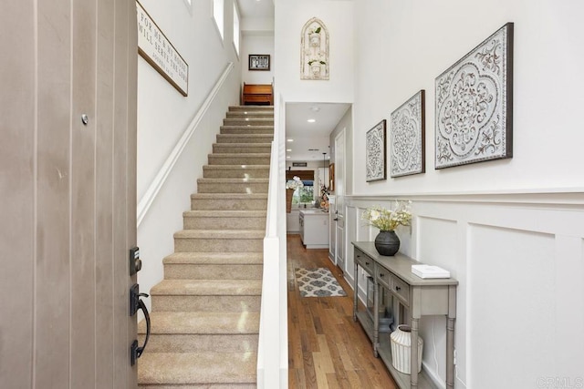 stairs with recessed lighting, a high ceiling, and wood finished floors