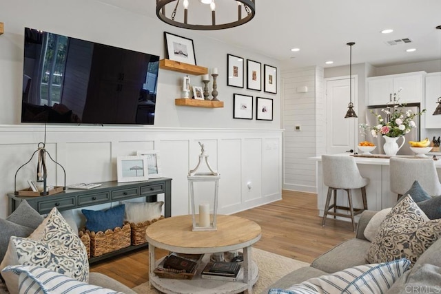 living area featuring recessed lighting, a wainscoted wall, visible vents, a decorative wall, and wood finished floors