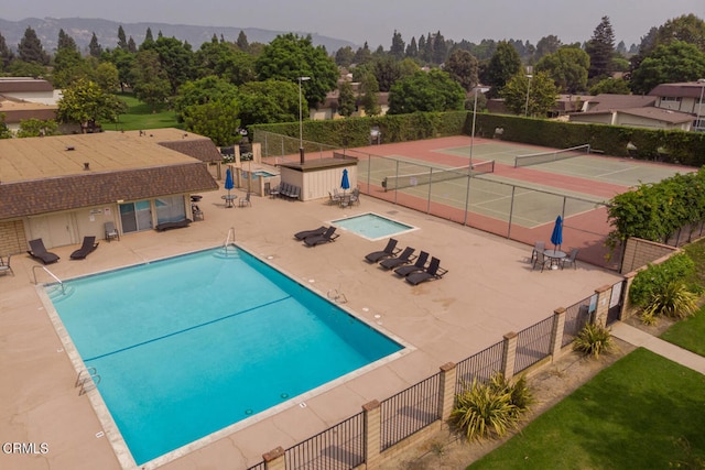 community pool featuring a tennis court, fence, and a patio