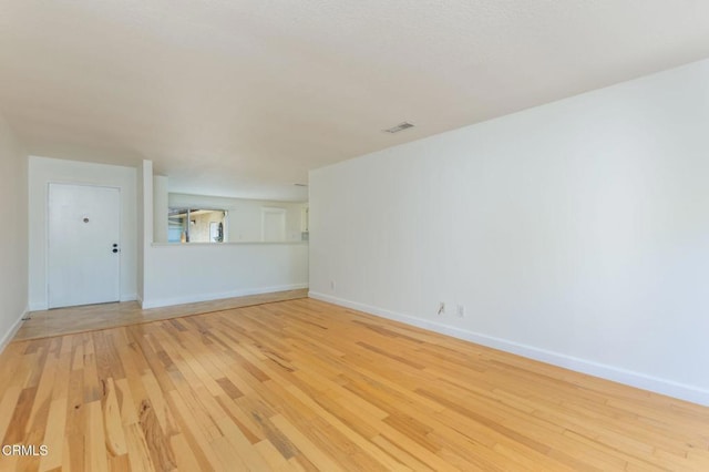 empty room featuring baseboards, light wood finished floors, and visible vents