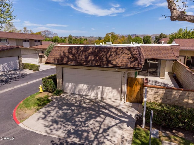 view of front of property with roof with shingles, concrete driveway, fence, and mansard roof