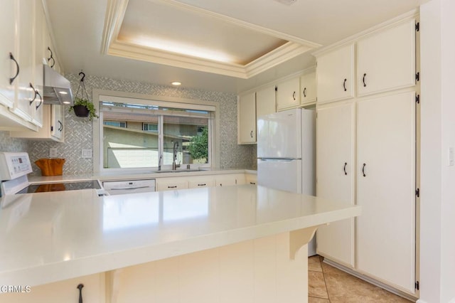 kitchen featuring a sink, a tray ceiling, white appliances, under cabinet range hood, and decorative backsplash