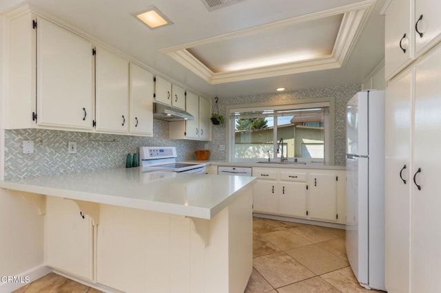 kitchen with a sink, a peninsula, white appliances, under cabinet range hood, and a raised ceiling