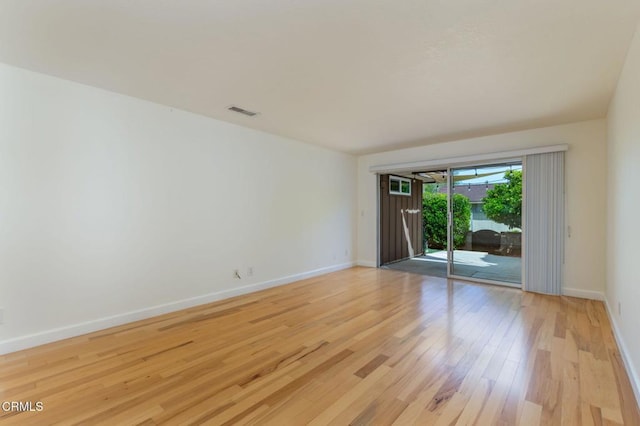 empty room with light wood finished floors, visible vents, and baseboards