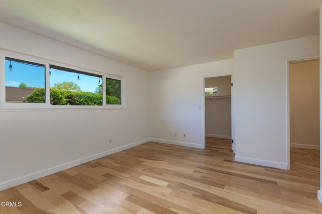 unfurnished bedroom with baseboards, light wood finished floors, a closet, and a walk in closet